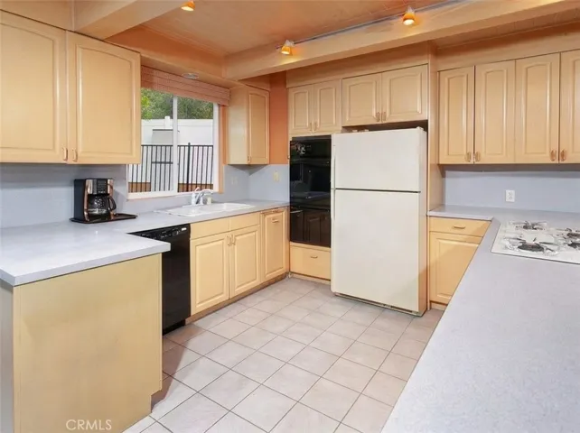 The kitchen is warm and inviting, offering generous cabinetry, a breakfast bar for casual dining, a pantry, and a dedicated coffee bar area. It is equipped with a built-in Maytag oven, gas cooktop, Whirlpool dishwasher, and a window over the sink that fills the space with natural light, making it a comfortable place to cook and gather.