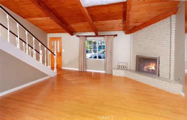 Light-filled living room featuring a striking floor-to-ceiling raised hearth brick fireplace, wood flooring, and high-pitched wood plank ceilings with exposed beams and a skylight that brings in abundant natural light. French doors provide a seamless connection to the dining area and kitchen.