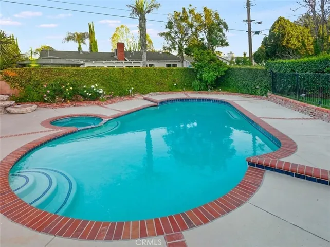 The backyard offers a private and inviting setting designed for relaxation and enjoyment, featuring a fenced in-ground pool and spa, covered and open patio areas, a grassy lawn, and raised brick planters with roses. A mature shade tree, outdoor lighting, and a garden shed enhance the space, while the side yard with artificial grass and a mini putting green adds a fun and functional touch.