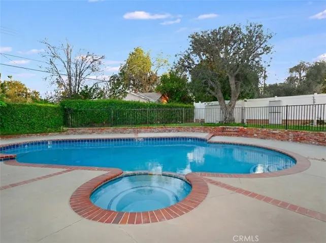 The backyard offers a private and inviting setting designed for relaxation and enjoyment, featuring a fenced in-ground pool and spa, covered and open patio areas, a grassy lawn, and raised brick planters with roses. A mature shade tree, outdoor lighting, and a garden shed enhance the space, while the side yard with artificial grass and a mini putting green adds a fun and functional touch.