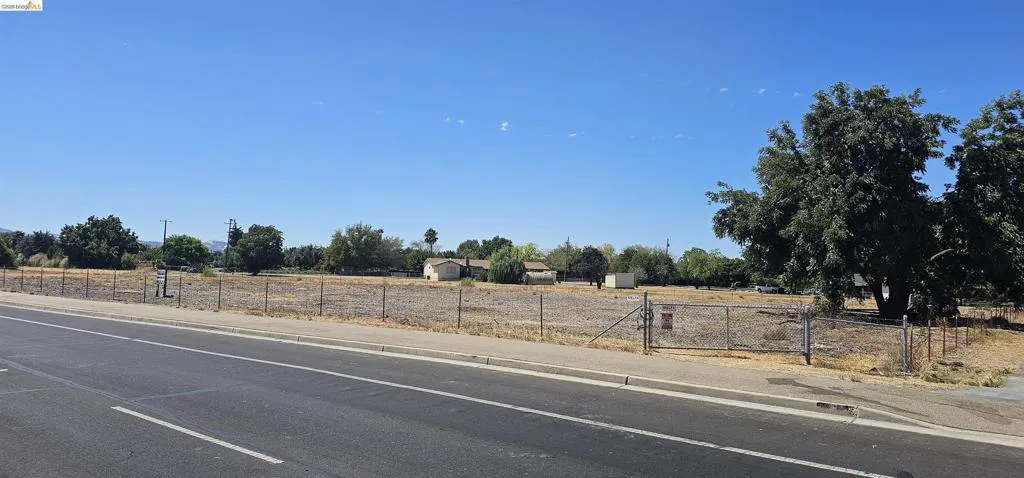 View of asphalt road with sidewalks, a gate, a view of countryside, and curbs