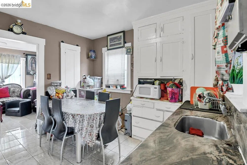 Kitchen with white cabinets, white microwave, light tile patterned floors, and dark stone counters