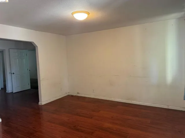 Spacious room featuring wood-finish flooring, white baseboards, and an overhead flush-mount light fixture