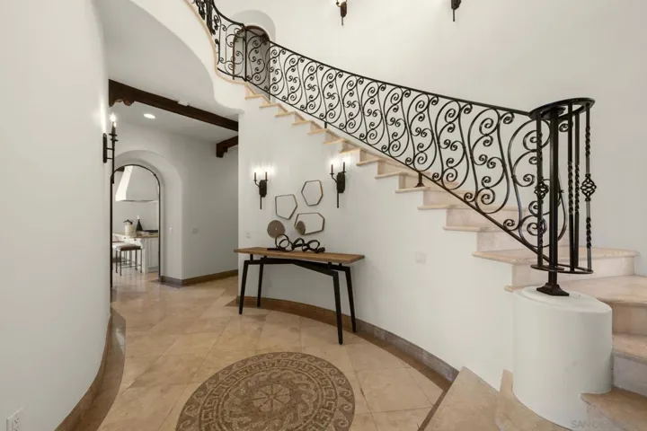Gracious entry anchored by a sweeping custom iron staircase, where artisan tile underfoot and soft architectural curves create an elegant, gallery-like welcome.