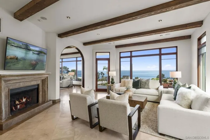 Family room with exposed wood beams, ocean views, and a beautiful fireplace, where walls of glass fill the space with light and create a warm, inviting setting for relaxed coastal living.