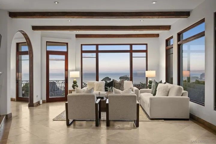 Family room with exposed wood beams and expansive windows framing panoramic ocean views, where natural light and coastal warmth create an inviting space for gathering and relaxation.