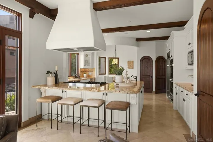 Gourmet kitchen with rounded door frames, island seating, a custom hood, and stone countertops, where thoughtful design and warm finishes create an inviting space for both everyday living and elevated entertaining.
