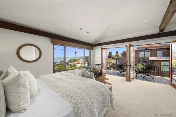 Primary bedroom oriented toward double French doors that open to a private balcony, where natural light and ocean air create a seamless extension of the retreat beyond.