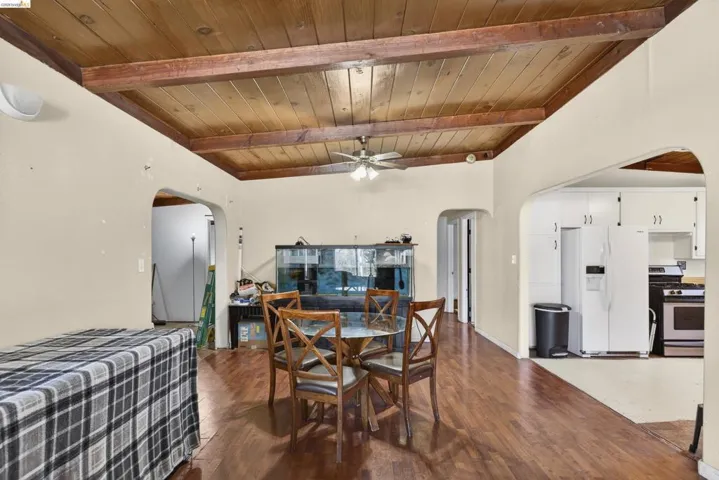 Dining room featuring arched walkways, dark wood finished floors, a ceiling fan, and a wood ceiling with exposed beams