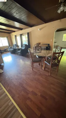 Spacious interior featuring wood-finish flooring, a beamed ceiling, and multiple windows with dark​​‌​​​​‌​​‌‌​​‌​​​‌‌​​​‌​​‌‌​​‌‌​​‌‌​​​​ drapery