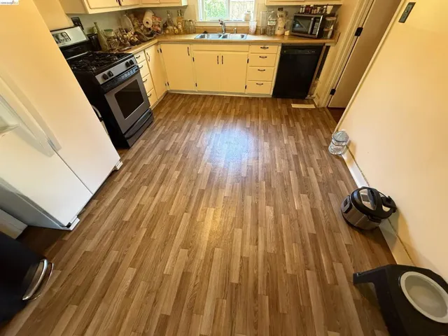 Kitchen featuring wood-finish flooring, white cabinetry, a double basin sink, and a black range