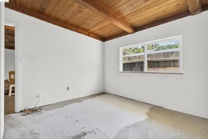 Spare room featuring a wooden ceiling with exposed beams and unfinished concrete flooring