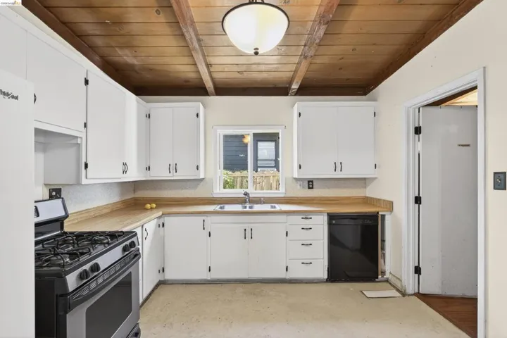 Kitchen featuring light countertops, gas stove, black dishwasher, white cabinetry, and concrete floors