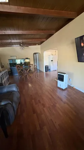 Open-concept interior featuring wood-finish flooring, exposed wood beam ceiling, and a wide arched entryway