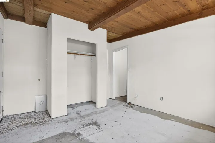 Unfurnished bedroom featuring a wooden ceiling with exposed beams, concrete flooring, and a closet