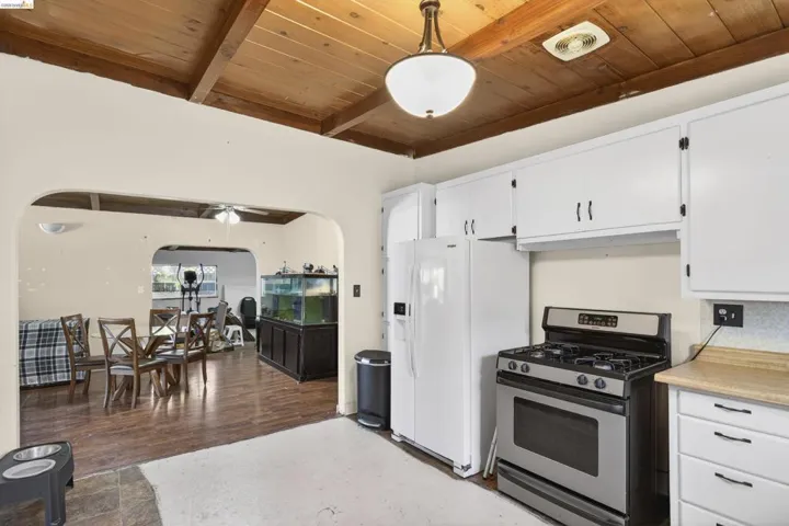 Kitchen with stainless steel gas range, light countertops, arched walkways, white cabinets, and a wood ceiling with exposed beams