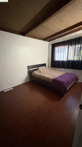 Room featuring wood-finish flooring, white walls, and a window with dark privacy curtains