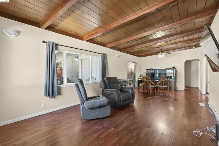 Living area with a wooden ceiling with exposed beams, arched walkways, wood finished floors, and a ceiling fan