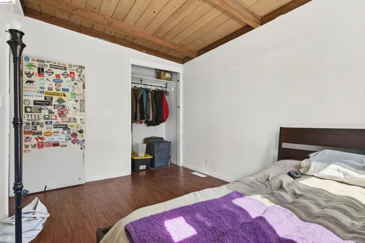 Bedroom with a closet, a wooden ceiling with exposed beams, and dark wood finished floors