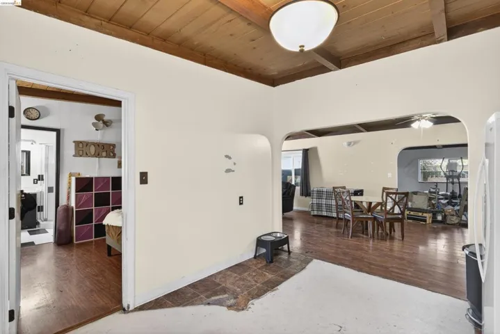 Living area with a wooden ceiling with exposed beams, arched walkways, wood finished floors, and ceiling fan
