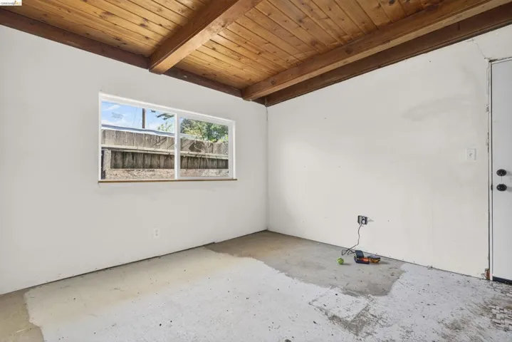 Empty room with a wood ceiling with exposed beams and concrete flooring