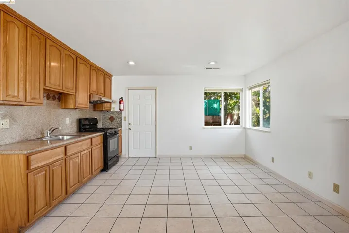 Kitchen with black range with gas cooktop, wood finish cabinetry, backsplash, light tile patterned floors, and recessed lighting