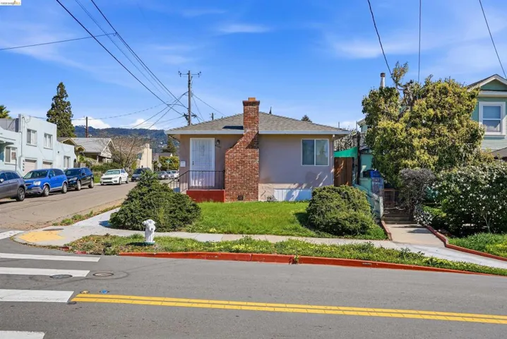 Bungalow-style home with stucco siding, a shingled roof, a chimney, a residential view, and a front lawn
