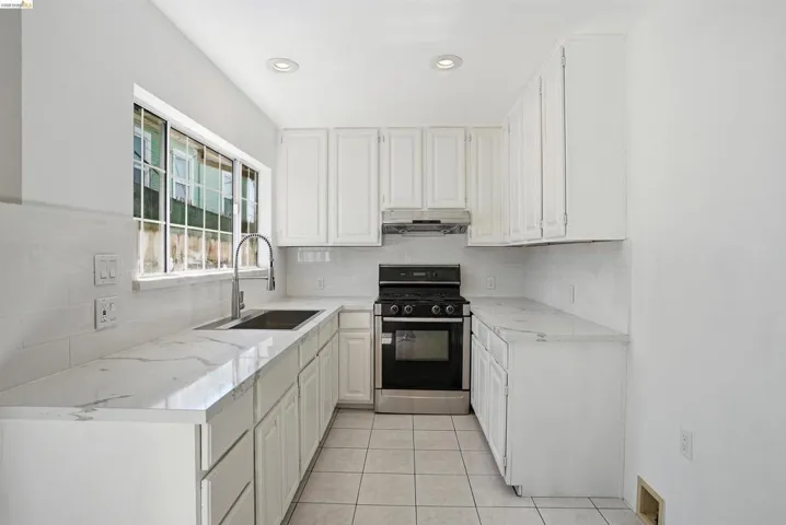 Kitchen featuring black range with gas stovetop, white cabinetry, backsplash, light stone counters, and recessed lighting