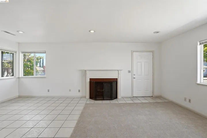 Unfurnished living room featuring light tile patterned floors, a fireplace with flush hearth, recessed lighting, and light carpet