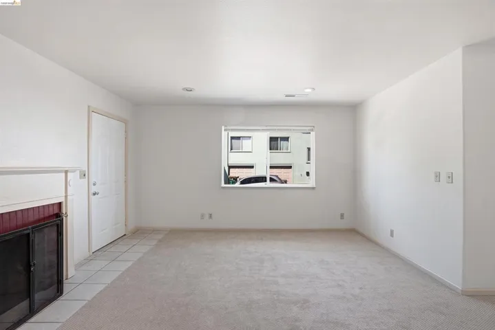 Unfurnished living room featuring a brick fireplace, light colored carpet, and light tile patterned flooring