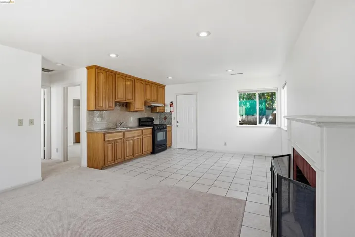 Kitchen with black gas stove, wood finish cabinetry, light tile patterned floors, a fireplace with flush hearth, and decorative backsplash