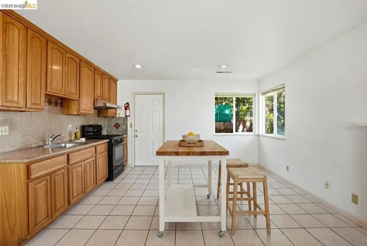 Kitchen featuring wood finish cabinetry, black gas range oven, decorative backsplash, light tile patterned flooring, and recessed lighting