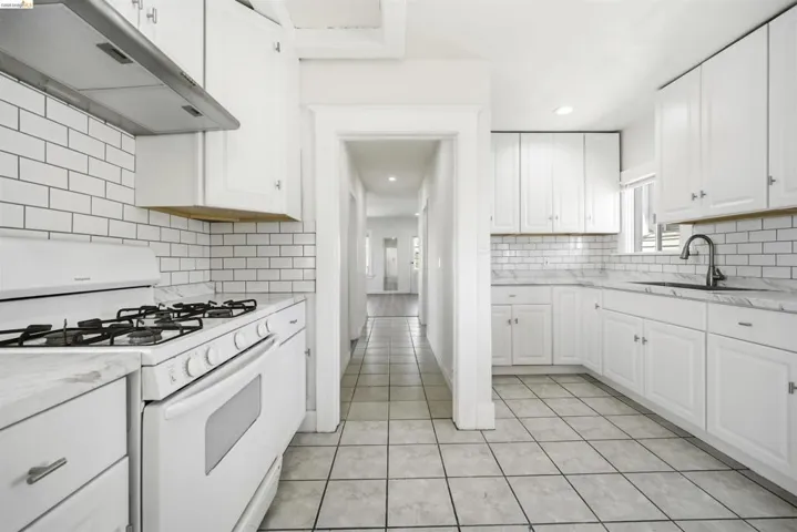 Kitchen with white range with gas stovetop, white cabinetry, recessed lighting, light stone counters, and light tile patterned floors