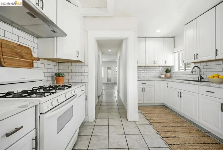 Kitchen featuring white range with gas stovetop, light stone countertops, white cabinets, recessed lighting, and light tile patterned flooring