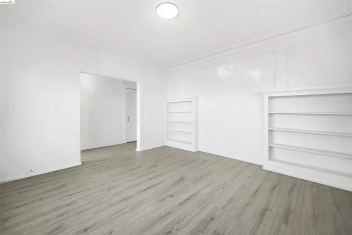 Empty room with built in shelves, ornamental molding, and light wood-style flooring