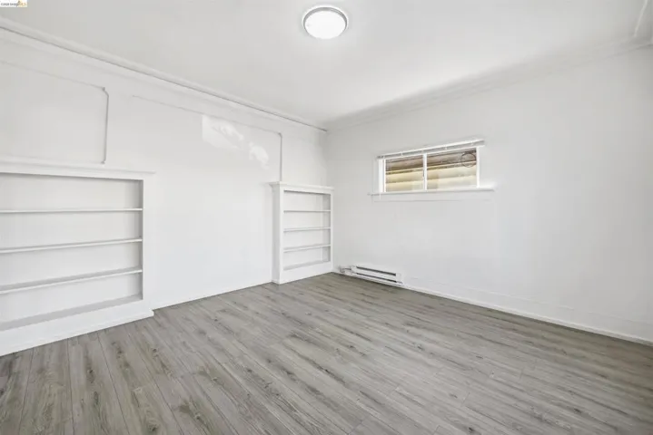 Spare room featuring light wood-type flooring, ornamental molding, a baseboard heating unit, and built in features