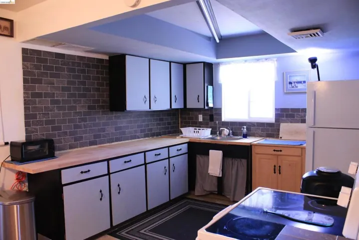 Kitchen featuring freestanding refrigerator, two tone color scheme, backsplash, and wood counters