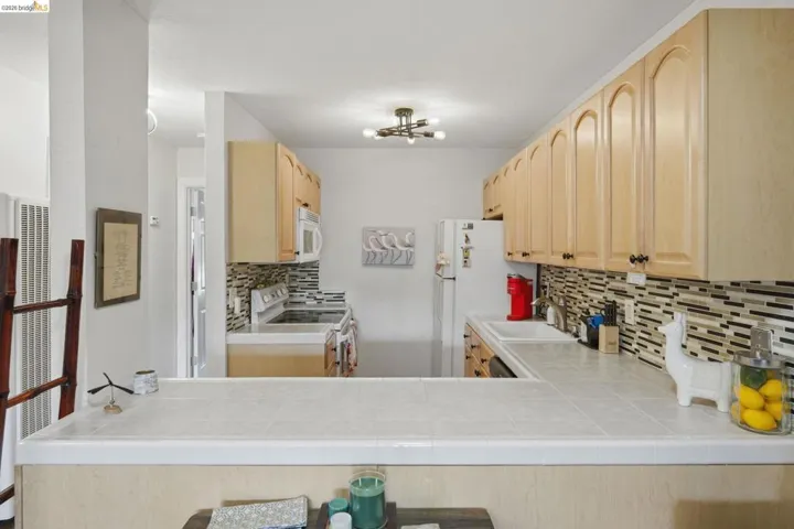 Kitchen with light wood finish cabinetry, tile counters, white appliances, and decorative backsplash