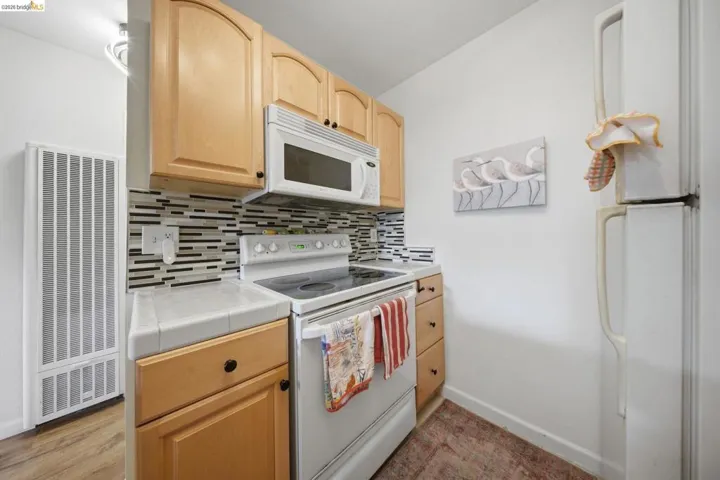 Kitchen featuring light wood finish cabinetry, white appliances, tile countertops, a heating unit, and backsplash
