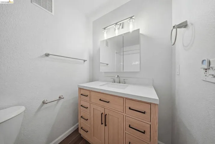 Half bathroom featuring a textured wall, vanity, and dark wood-style flooring