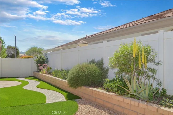 Easy-care backyard with covered patio with recessed lighting and roller shade; newly-installed, pet-friendly artificial lawn; curved paver pathway; raised garden beds; and vinyl fencing