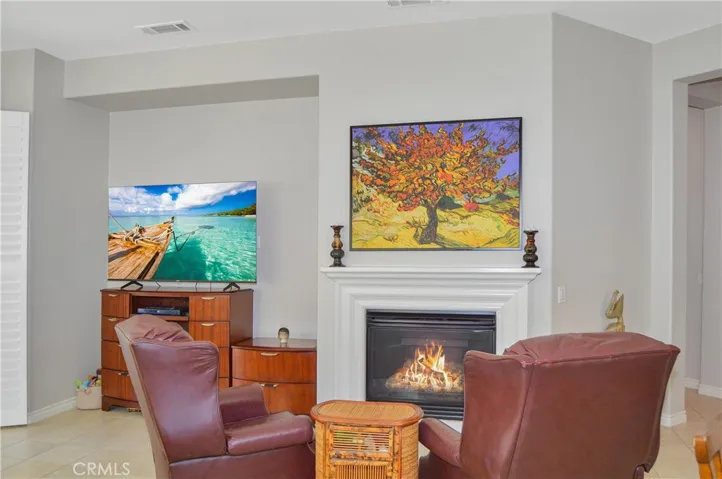 The great room offers the open floor plan living you desire with a cozy fireplace, louvered shutters, tile flooring, ceiling fan, and easy access to the covered patio out back. Fire in fireplace and TV image added virtually.
