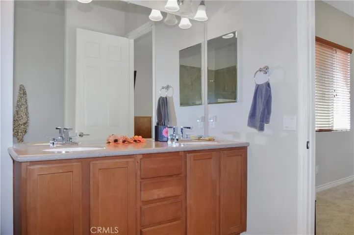 Primary bath with easy-access, walk-in, tiled shower with extra-tall dual shower heads; matching tile surround on soaking tub, dual sinks, Corian-style countertop, wood-look blinds, and tile flooring.