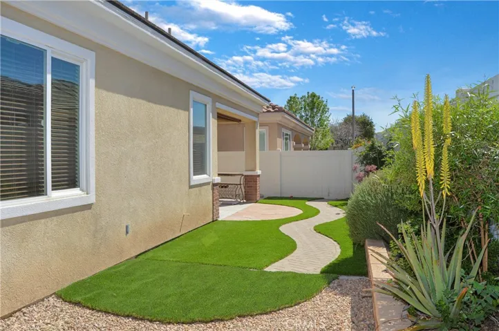 Easy-care backyard with covered patio with recessed lighting and roller shade; newly-installed, pet-friendly artificial lawn; curved paver pathway; raised garden beds; and vinyl fencing