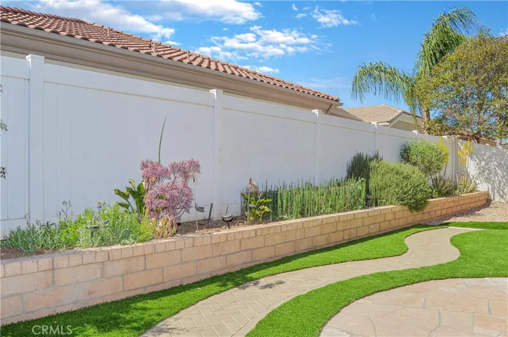 Easy-care backyard with covered patio with recessed lighting and roller shade; newly-installed, pet-friendly artificial lawn; curved paver pathway; raised garden beds; and vinyl fencing