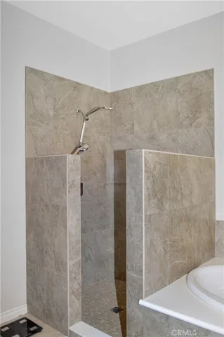 Primary bath with easy-access, walk-in, tiled shower with extra-tall dual shower heads; matching tile surround on soaking tub, dual sinks, Corian-style countertop, wood-look blinds, and tile flooring.