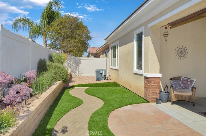 Easy-care backyard with covered patio with recessed lighting and roller shade; newly-installed, pet-friendly artificial lawn; curved paver pathway; raised garden beds; and vinyl fencing
