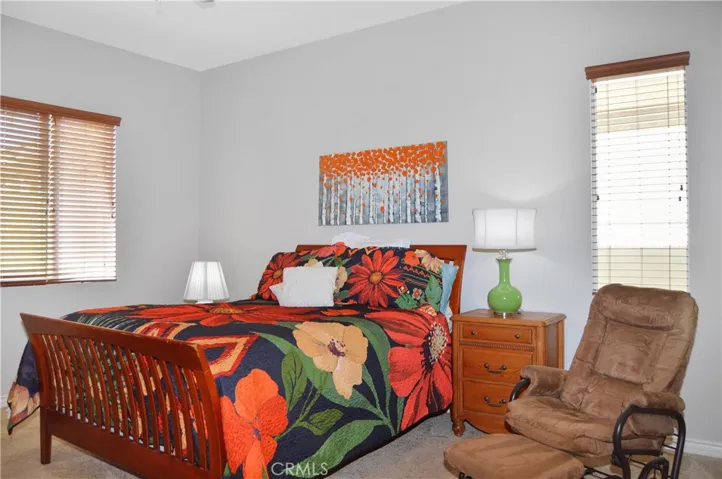 Primary bedroom suite with wood-look blinds, cozy carpet, a ceiling fan, a spacious walk-in closet and an en suite bath.