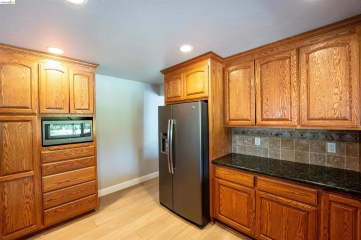 Kitchen with stainless steel fridge with ice dispenser, backsplash, wood finish cabinets, light wood finished floors, and dark stone counters