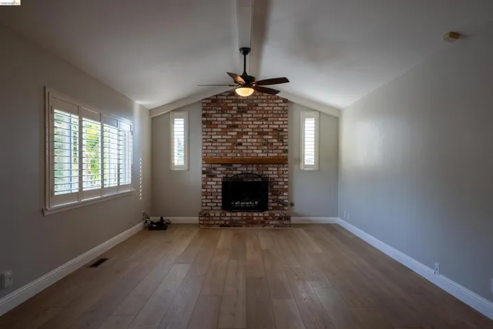 Unfurnished living room featuring hardwood / wood-style flooring, ceiling fan, a brick fireplace, and beamed ceiling